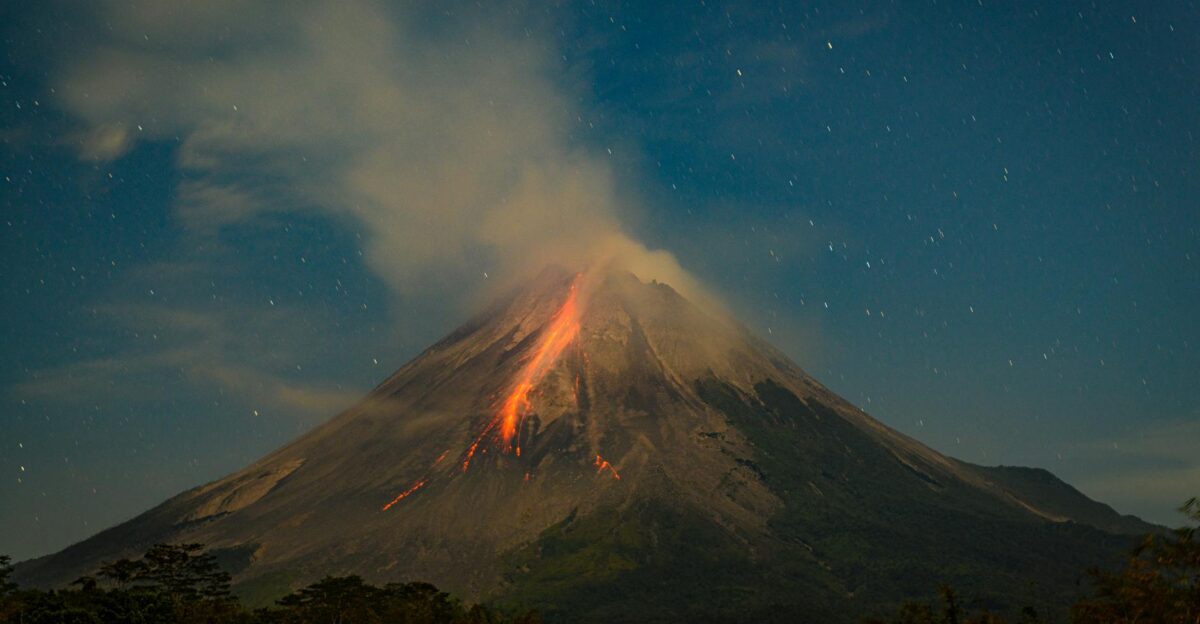 A nighttime view of a volcanic eruption with glowing lava and a starry sky