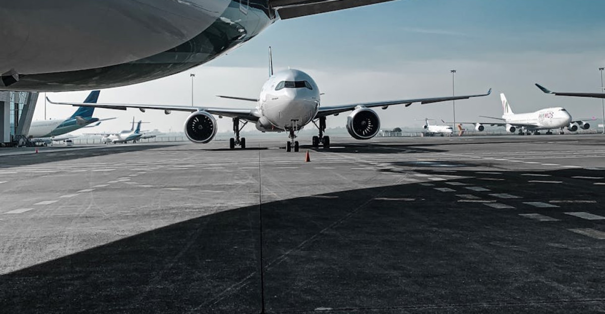 Low angle of various airplanes parked on airfield against blue sky on sunny day